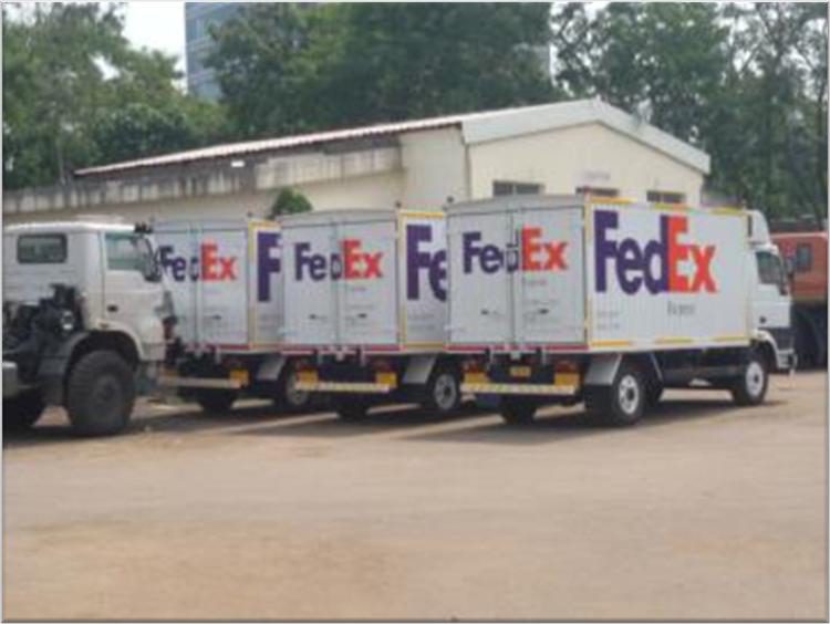 Row of FedEx box trucks with full livery graphics and reflective conspicuity strips